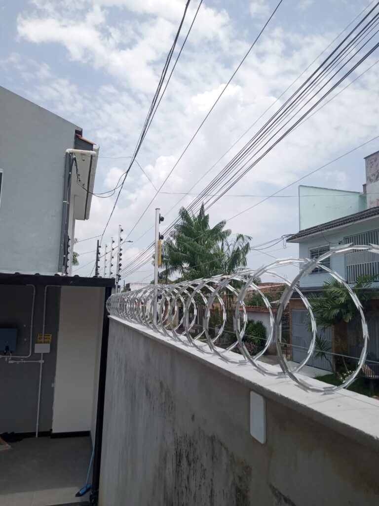 Muro de casa nova com espiral de concertina e hastes de cerca elétrica alinhadas ao longo da rua