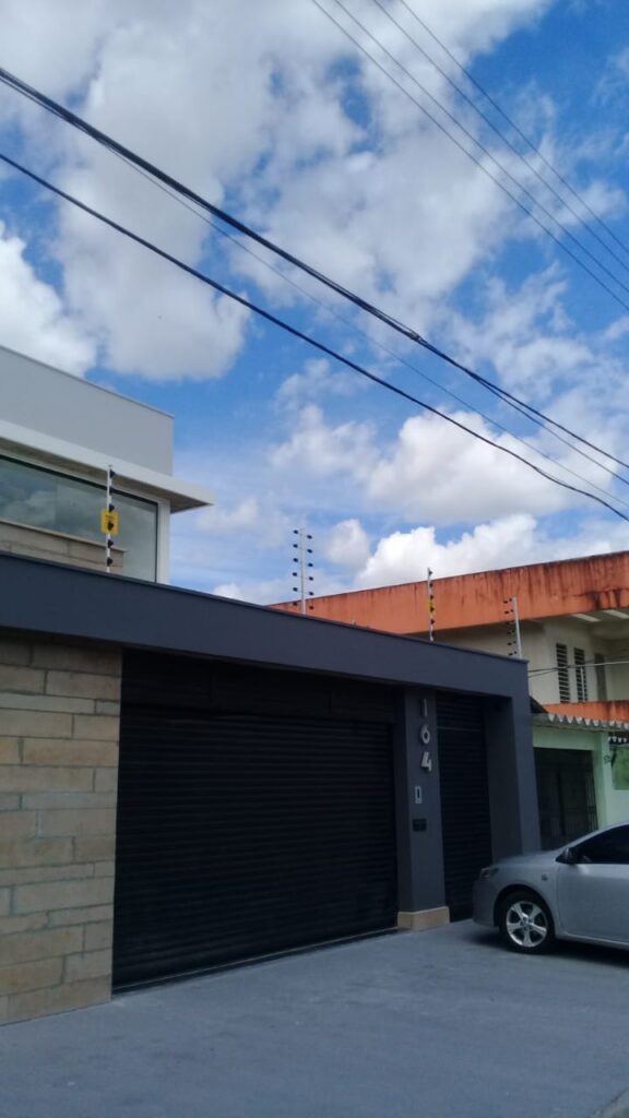 Fachada moderna com portão de enrolar preto e hastes discretas de cerca elétrica no alto do muro